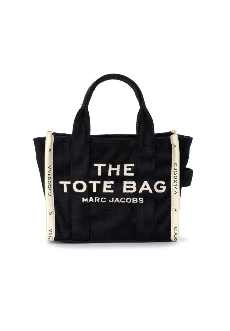 Geantă de tote din pânză neagră cu text alb care citește „THE TOTE BAG MARC JACOBS.” Are mânere scurte și accente albe contrastante.