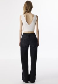 Witte geribbelde crop top met een diepe V-rugontwerp, gecombineerd met hoge zwarte spijkerbroeken met een gestructureerde stof en een wijde pijp.