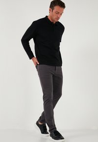 Crna polo majica dugih rukava i sive slim-fit hlače, uparene s crno-bijelim tenisicama. Glatka tkanina s ležernim krojem.