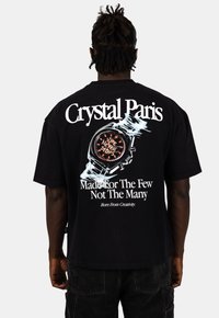 Černé bavlněné tričko s potiskem hodinek a textem "Čas nikdy nezastavuje" a "Crystal Paris" v tučném bílém písmu na zadní straně.