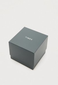 Caixa fechada de relógio Timex cinza com logotipo branco sobre um fundo claro.