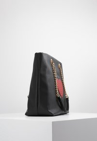 Svart konstläder tote-väska med röd hjärtdetalj, guldkedjeaxelremmar, strukturerad form och slät yta.