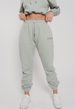 Mint green sweatpants with an elastic waistband and cuffs, featuring a drawstring and embossed logo on the side, paired with white sneakers.