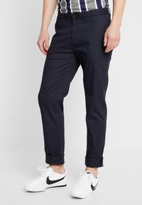 Marineblå chinos med slim fit og opbrettede cuffs, lavet af letvægtsstof. Sammen med hvide Nike sneakers med et sort swoosh-logo.