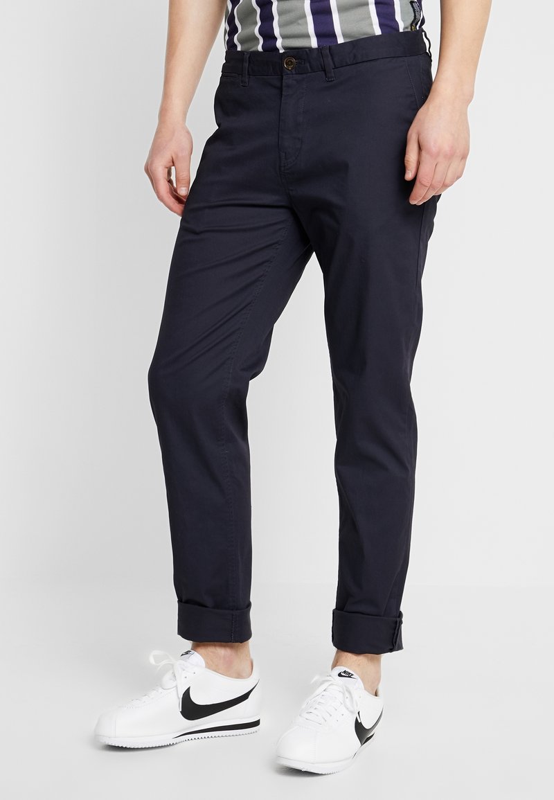 Marineblå chinos med slim fit og opbrettede cuffs, lavet af letvægtsstof. Sammen med hvide Nike sneakers med et sort swoosh-logo.