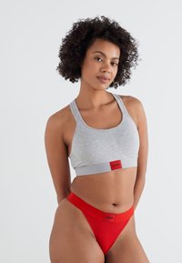 Hallhallik liigspordirinnahoidja punase elastse riba- ja logoga, koos punaste stringide aluspükstega. Sile kangas, lihtne disain, mugav sobivus.
