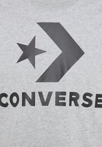 Logo Converse avec une étoile noire et un chevron au-dessus de lettres noires en gras sur un fond en tissu gris.