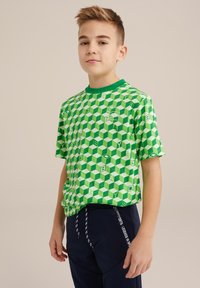 Zaļa īsa piedurkne T-krekls ar 3D kuba rakstu, apaļu kakla izgriezumu un diskreṭu logo, kombinēts ar tumši ziliem biksēm ar ievelkamu auklu.