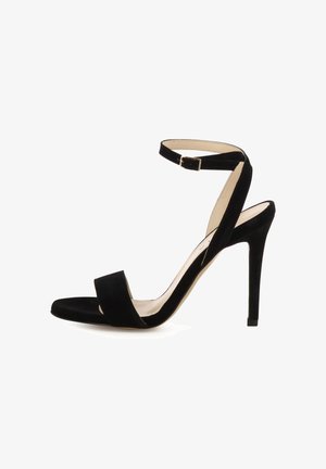 Sandalo con tacco alto in suede nero con cinturino alla caviglia e fibbia, punta aperta e sottile tacco a spillo su sfondo bianco.