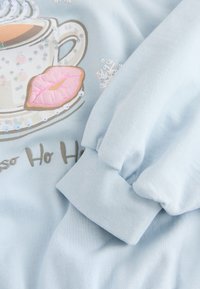 Svetlo modra jopa s potiskom skodelice za kavo z bleščicami, dizajnom rožnatih ustnic in napisom "Ho Ho Ho" v igrivem fontu.