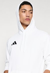 Λευκό φούτερ με κορδόνι, που φέρει ένα μαύρο λογότυπο με τρεις ρίγες στο αριστερό στήθος. Μαλακό ύφασμα με άνετη εφαρμογή.