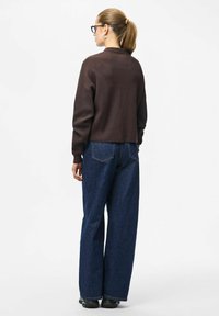 Brązowy krótki sweter w połączeniu z szerokimi, ciemnoniebieskimi dżinsami. Modelka z kucykiem nosi czarne buty i duże kolczyki.