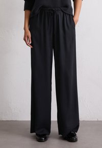Zwarte, wijde broek met een trekkoord in de taille, gemaakt van een gladde, lichte stof. Heeft zijzakken en een losse pasvorm.