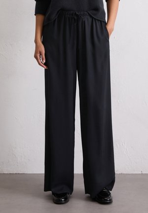 Zwarte, wijde broek met een trekkoord in de taille, gemaakt van een gladde, lichte stof. Heeft zijzakken en een losse pasvorm.