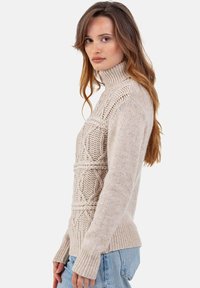 Pull beige clair en tricot avec un col montant, des motifs texturés et des manches longues. Comprend des poignets et un ourlet côtelés pour un confort accru.