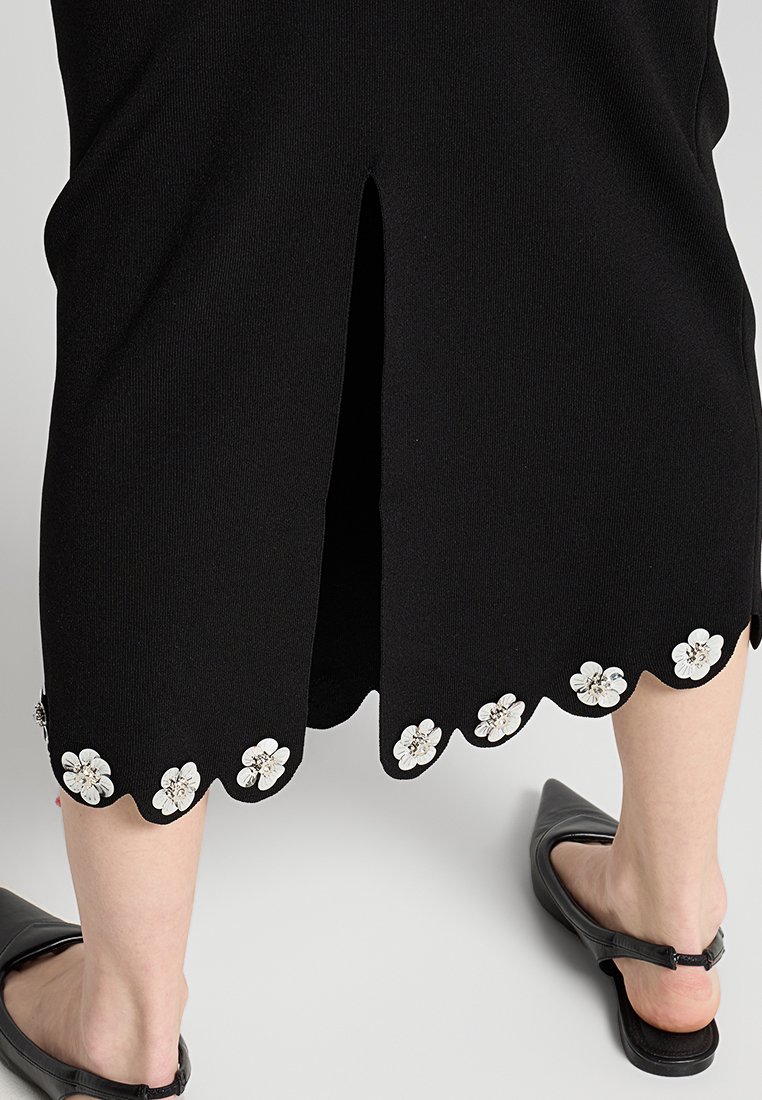 Schwarzes Rippstrickkleid mit einem Rückenschlitz, das einen gewellten Saum mit weißen Blumenapplikationen und silbernen Akzenten verziert.