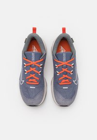 Niebieskie buty sportowe z teksturowaną siateczką u góry, pomarańczowymi sznurówkami, wyściełanym kołnierzem i białą podeszwą z wzorzystymi akcentami.