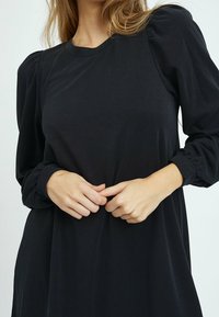 Svart långärmad klänning med rund halsringning och puffärmar. Mjukt tyg, avslappnad passform och subtila veck i midjan.