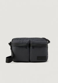 Μαύρο τσαντάκι χιαστί με δύο μπροστινές τσέπες, ρυθμιζόμενο λουράκι και ετικέτα με το λογότυπο Tommy Hilfiger στο κάτω δεξί μέρος.