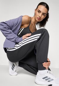 Sporty antrekk med en grå tanktop og matchende joggebukser med hvite striper, komplettert med en lavendel oversized jakke og hvite sneakers.