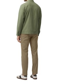 Groene jas van textuurstof, gecombineerd met tan kleurige broeken en witte sneakers met zwarte accenten. Zicht van achteren.