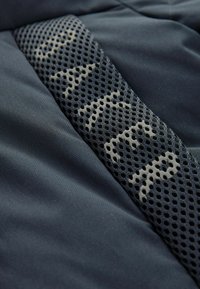 Crna i tamnoplava tkanina s reljefnom mrežastom panelom koji sadrži uzorak i svijetle naglašene boje. Općenito mekana i glatka tekstura.