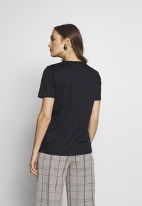 Schwarzes Kurzarm-T-Shirt mit Rundhalsausschnitt, kombiniert mit grauen karierten Hosen mit einem Karomuster. Der Stoff scheint glatt zu sein.