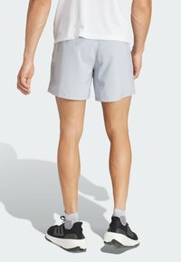 Shorts deportivos de color gris claro con un acabado suave, combinados con zapatillas en blanco y negro con una suela texturizada y calcetines grises.