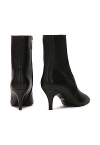 Botas de cuero negro hasta el tobillo con punta afilada, tacón alto y delgado, y cremallera lateral. Textura suave con detalles de costura mínimos.