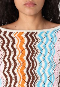 Stickad tröja med ett zigzag-mönster i brunt, orange, blått, vitt och rosa. Öppen vävstruktur med en off-the-shoulder halsringning.