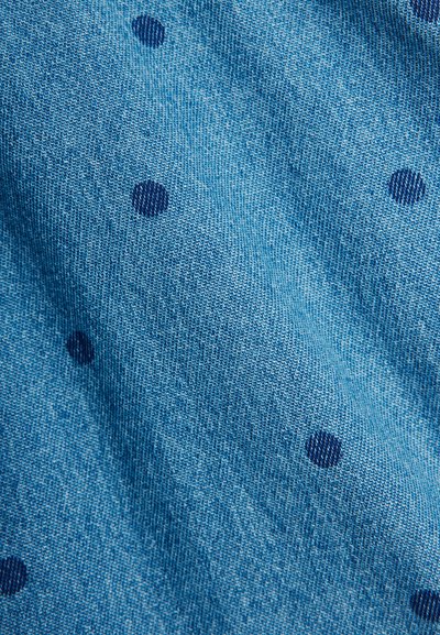 Μπλε πλεκτό ύφασμα με σχέδιο από μικρές σκούρες μπλε πουά, που εμφανίζει υφή και ελαφριές πτυχώσεις.