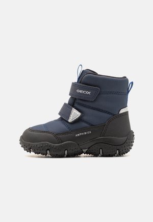 Botte d'hiver imperméable pour enfant en bleu marine et noir, avec deux sangles réglables, semelle texturée et boucles de traction au niveau de la cheville et du talon.