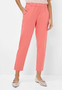 Koraalkleurige, lichte broeken met een elastische tailleband, zijzakken en taps toelopende pijpen. Gecombineerd met zilveren ballet flats met een strikaccent.