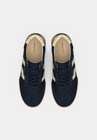 Τα Navy και cream αθλητικά παπούτσια διαθέτουν σχεδιασμό από σουέντ και ύφασμα, με στρογγυλή μύτη, επίπεδα κορδόνια και καφέ λάστιχο στη σόλα. Το λογότυπο GANT είναι ορατό στο εσωτερικό.
