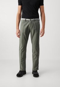 Pantalon en coton vert clair à coupe droite, avec des poches avant et une passoire de ceinture noire. Assorti à des chaussures de sport noires.