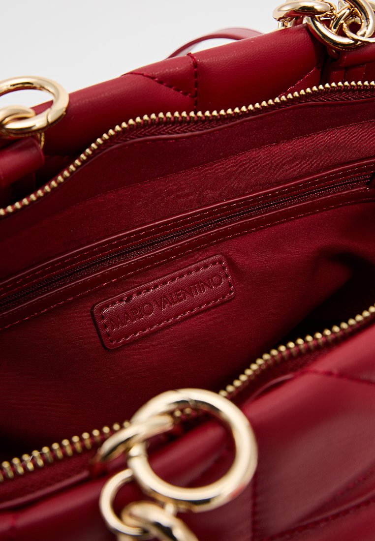Sac à main rouge avec un design matelassé, accents en métal doré et poche zippée intérieure. Équipé d'une étiquette de logo et d'une doublure en tissu lisse.