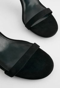 Sandali neri con tacco caratterizzati da una tomaia in pelle liscia e una fascia in suede sulla punta. Il design include una forma curva e linee eleganti.