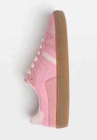 Baskets roses avec une tige en cuir suédé et lisse, ornées de rayures blanches et de lacets, et une semelle en caoutchouc marron texturée.