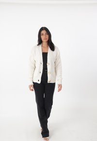 Gebreide cardigan in gebroken wit met een textuurpatroon, voorzien van grote gouden knopen, geribde manchetten en een open voorkant. Gecombineerd met zwarte broek.