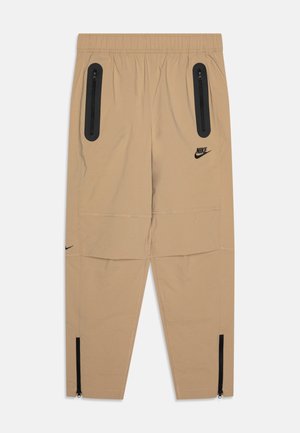 Pantaloni Nike beige con cintura regolabile a cordoncino, due tasche nere con zip e cerniere alle caviglie per la regolazione. Presentano accenti logo sul davanti.