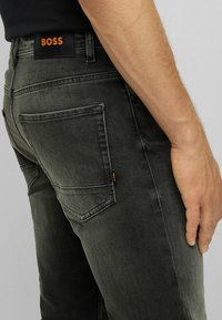 Dark grey denim jeans with a fitted design, featuring dual back pockets and an orange "BOSS" logo tab on the waistband.