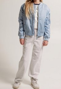 Giubbotto bomber azzurro chiaro con motivo trapuntato, abbinato a pantaloni della tuta grigi. Il completo presenta polsini a coste e tasche con cerniera.