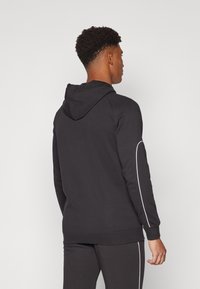 Black hooded sweatshirt with white accent lines on the sides, made of soft material, featuring a relaxed fit and ribbed cuffs and hem.