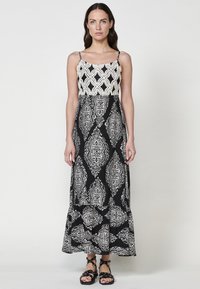 Robe maxi à motif noir et blanc avec un décolleté carré, des bretelles fines et un corsage ajusté qui se transforme en jupe fluide.