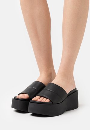Black platform sandals with wide upper bands. Made of synthetic material, they feature a smooth texture and a contoured wedge shape.