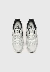 Baskets de running blanches avec un dessus en mesh, des accents noirs, un col rembourré et une semelle noire texturée avec des lacets et une marque sur la languette.