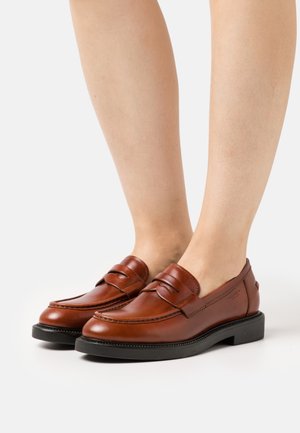 Mocassins en cuir marron avec une légère brillance, dotés d'un bout arrondi, d'une sangle décorative à l'avant et d'une semelle en caoutchouc noire.