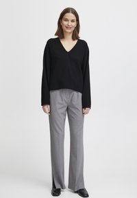 Pull noir à col en V avec des manches longues, associé à un pantalon taille haute gris clair avec des fentes latérales, et des chaussures noires.
