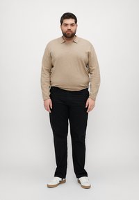 Beige polo triko s dlouhým rukávem a límečkem, v kombinaci s černými džíny a bílými teniskami s hnědými akcenty. Jednoduchý design, volný střih.