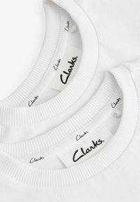 T-shirts blancs avec des cols ronds côtelés, comportant des étiquettes "Clarks" visibles sur les étiquettes intérieures. Texture de tissu simple et lisse.